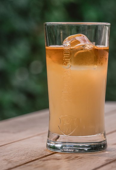 Ein Glas mit einem erfrischenden Getränk, das in sanften Gelb- und Orangetönen schimmert, steht auf einem Holztisch.