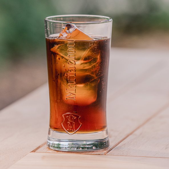 Maria Cola: Ein Glas mit einem erfrischenden Getränk, gefüllt mit Eiswürfeln und sprudelnden Blasen, steht auf einem Holztisch.