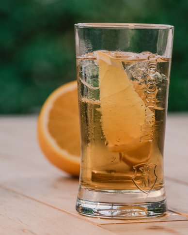 Ein Glas mit einem erfrischenden Getränk, gefüllt mit Eis und einer Zitronenscheibe, steht auf einem Holztisch.