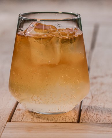 Ein Glas mit einem erfrischenden Getränk, gefüllt mit Eiswürfeln, steht auf einem Holztisch und sprudelt leicht.
