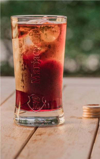 Das Glas zeigt eine erfrischende Mischung aus dunklen und hellen Flüssigkeiten, umgeben von einer natürlichen Umgebung.