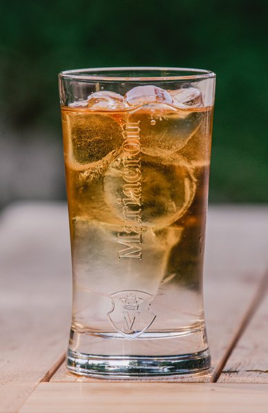 Ein Glas mit einem goldenen Getränk und Eiswürfeln steht auf einem Holztisch, im Hintergrund ist eine Flasche sichtbar.