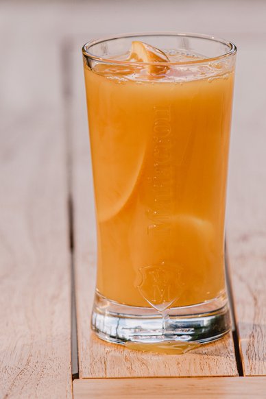 Ein Glas mit einem erfrischenden, orangefarbenen Getränk, garniert mit einer Scheibe Zitrone, steht auf einem Holztisch.