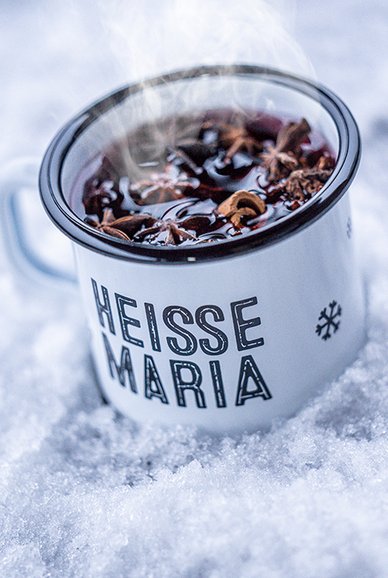 Ein dampfender Becher mit heißem Getränk steht auf frischem, weißem Schnee, umgeben von winterlicher Kälte.