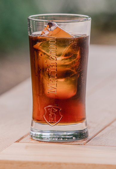 Maria Cola: Ein Glas mit einem erfrischenden Getränk, gefüllt mit Eiswürfeln und sprudelnden Blasen, steht auf einem Holztisch.