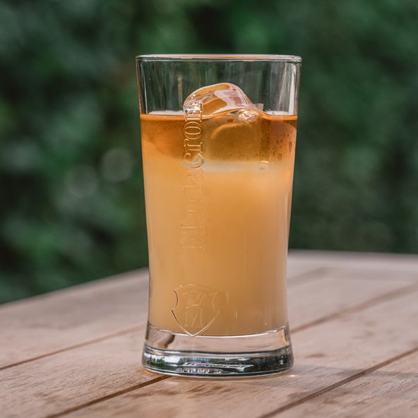 Ein Glas mit einem erfrischenden Getränk, das in sanften Gelb- und Orangetönen schimmert, steht auf einem Holztisch.