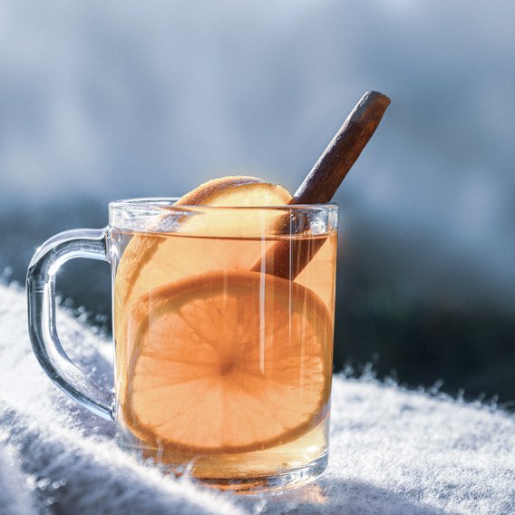 Ein Glas mit warmem Getränk, gefüllt mit orangefarbenem Tee, garniert mit einer Zimtstange und Orangenscheiben.