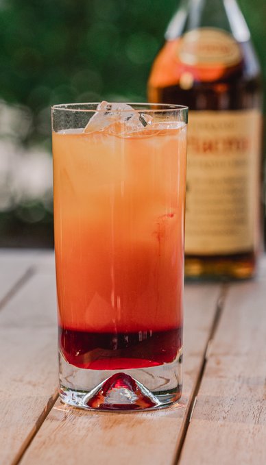 Ein erfrischendes Getränk in einem hohen Glas, mit Eiswürfeln und einer rot gefärbten Flüssigkeit, die sich darin vermischt.