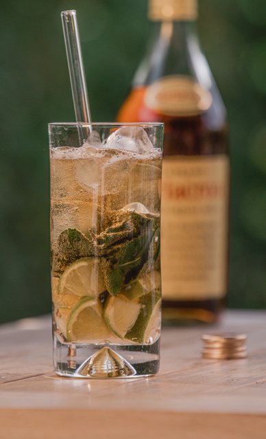 Ein Glas mit Eis, Limettenscheiben und frischer Minze wird mit einem sprudelnden Getränk gefüllt, während eine Flasche im Hintergrund sichtbar ist.