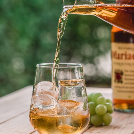 Ein Glas mit Eiswürfeln wird mit einem goldenen Getränk gefüllt, während eine Flasche im Hintergrund sichtbar ist.