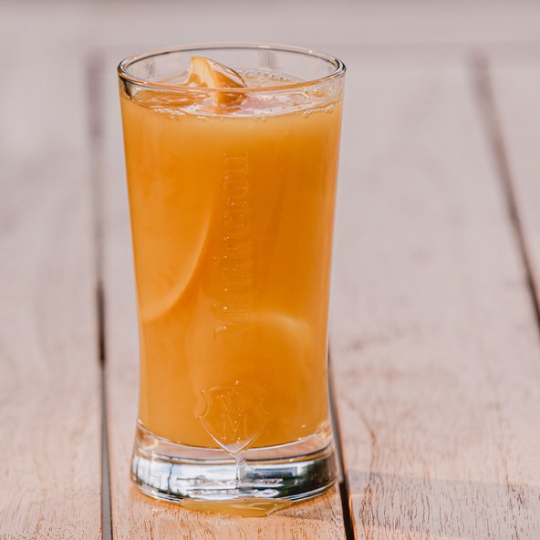 Ein Glas mit einem erfrischenden, orangefarbenen Getränk, garniert mit einer Scheibe Zitrone, steht auf einem Holztisch.