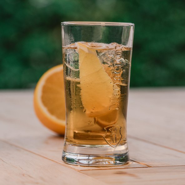 Ein Glas mit einem erfrischenden Getränk, gefüllt mit Eis und einer Zitronenscheibe, steht auf einem Holztisch.