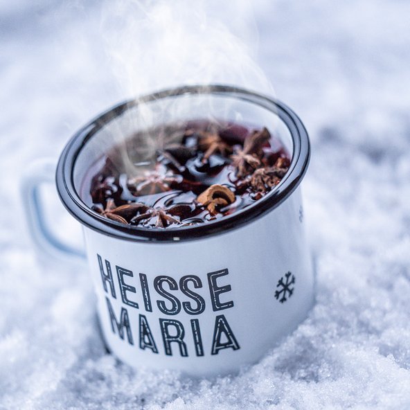 Ein dampfender Becher mit heißem Getränk steht auf frischem, weißem Schnee, umgeben von winterlicher Kälte.
