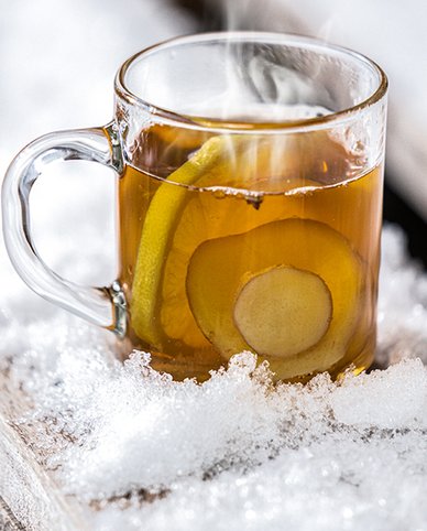 Ein dampfender Becher mit warmem Getränk steht auf einer Schneedecke, umgeben von frischen Zitronenscheiben.