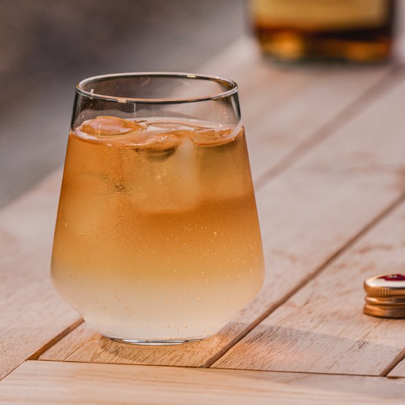 Ein Glas mit einem erfrischenden Getränk, gefüllt mit Eiswürfeln, steht auf einem Holztisch und sprudelt leicht.