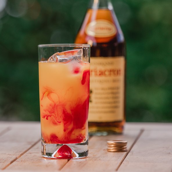 Ein erfrischendes Getränk in einem hohen Glas, mit Eiswürfeln und einer rot gefärbten Flüssigkeit, die sich darin vermischt.